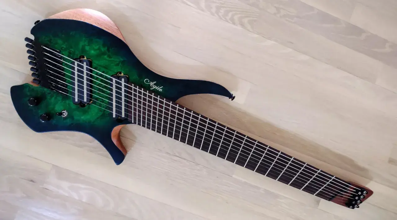 Guitare électrique Agile multiscale vert émeraude, avec 9 cordes et un manche fin, posée sur un parquet clair.