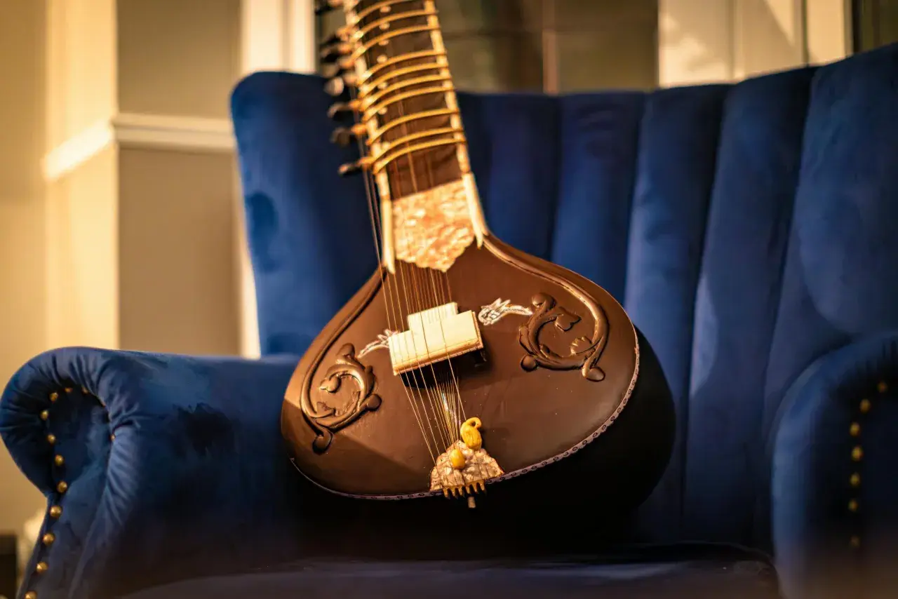 Un magnifique sitar indien repose sur un fauteuil bleu profond, prêt à faire vibrer ses cordes.