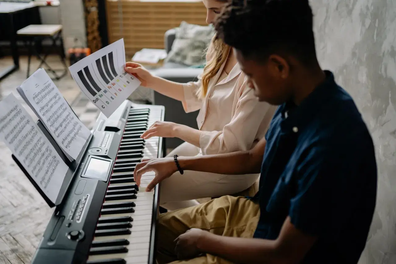 Deux mains jouent sur un piano, l'une suit une partition, l'autre une feuille avec des notes comme sol#m.