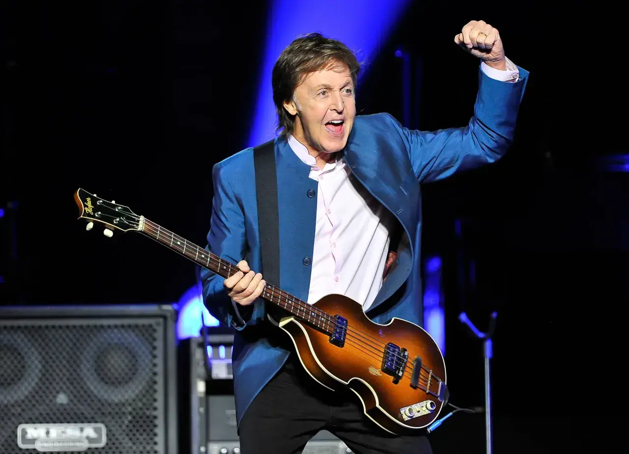 Paul McCartney, icône du rock, joue de sa basse Höfner sur scène, poing levé dans un geste d'enthousiasme.