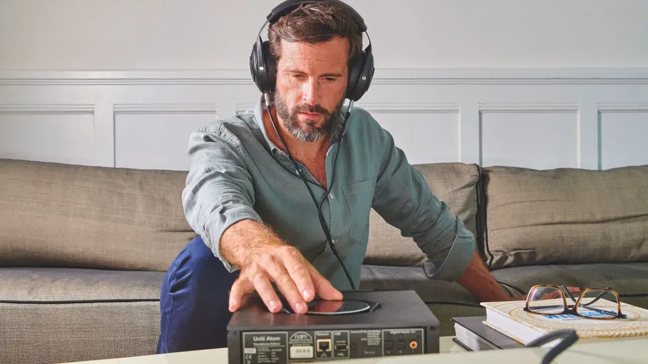 Homme concentré, casque audio sur les oreilles, ajustant un appareil. Il semble tester l'impédance de son casque audio pour une écoute parfaite.