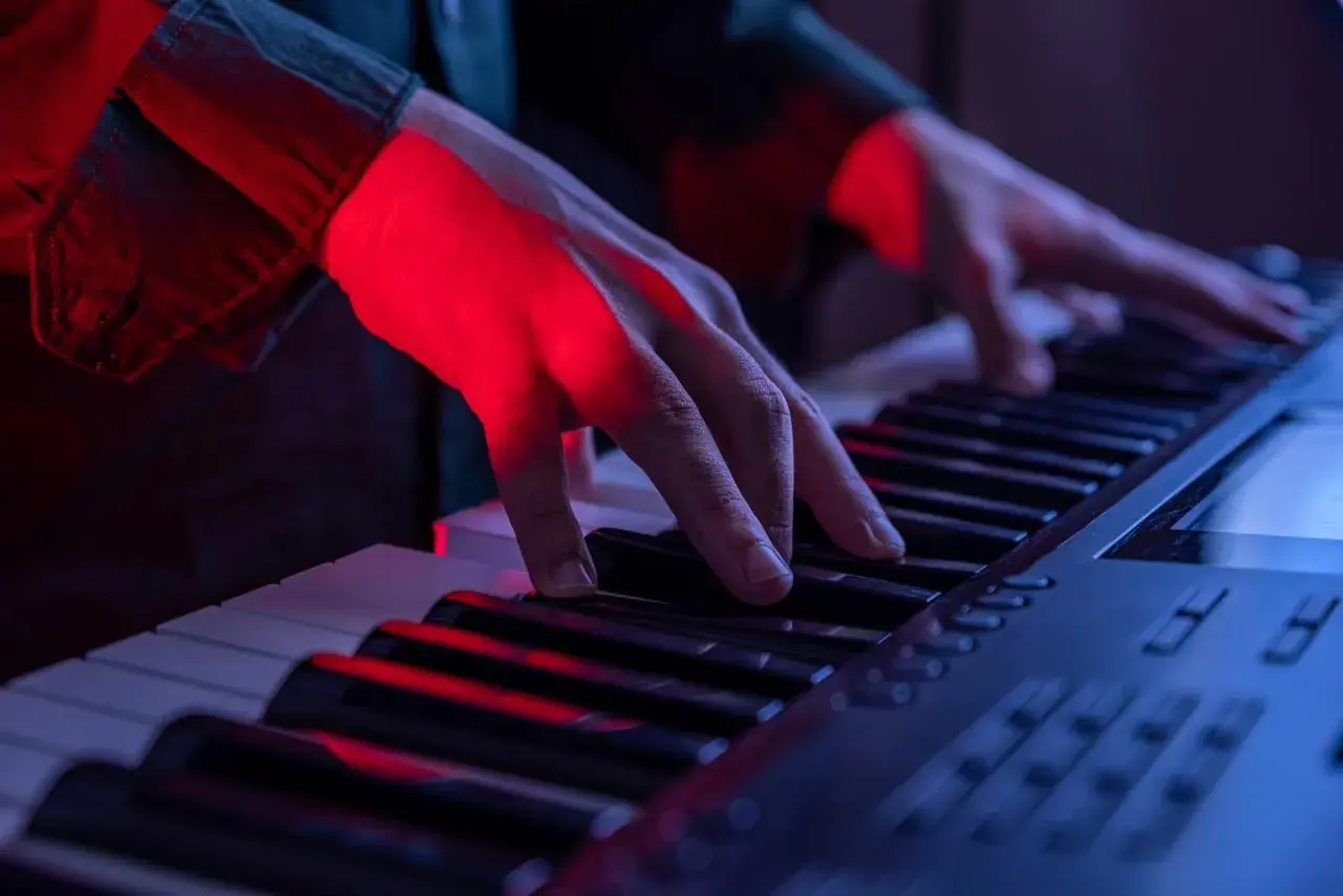 Mains éclairées par la lumière rouge jouant sur les touches d'un piano, créant une ambiance musicale.