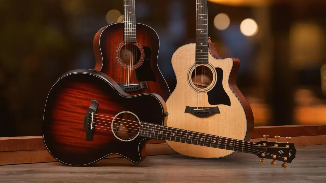 Trois guitares acoustiques, dont une en palissandre, posées sur un parquet en bois. L'arrière-plan est flou et lumineux.