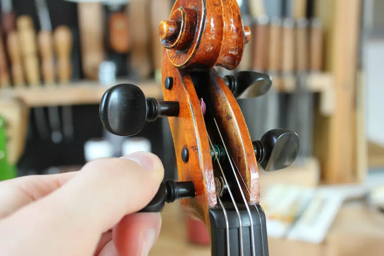 Main d'un musicien ajustant la tension d'une corde pour accorder le violon.