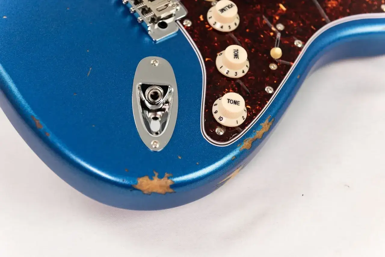 Guitare &eacute;lectrique bleue avec un aspect vieilli, montrant des &eacute;clats de peinture r&eacute;v&eacute;lant le bois. Le relicage guitare lui donne un charme vintage.