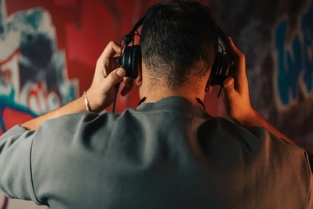 Un homme écoute de la musique avec des écouteurs, le mur derrière lui présente un micro-saignement de couleurs vives.
