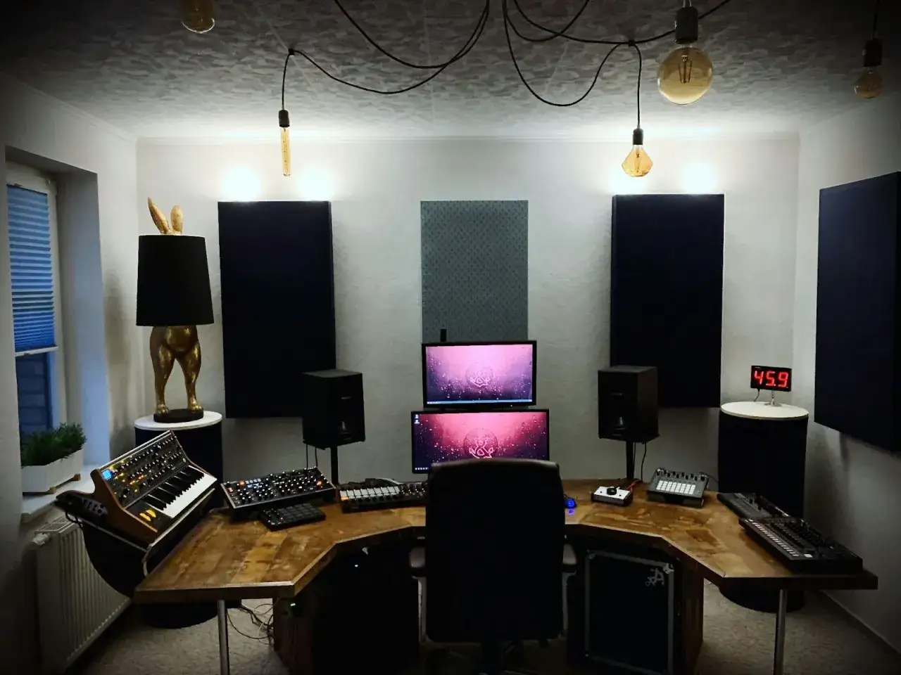 Studio d'enregistrement avec bureau en bois, claviers, &eacute;crans, enceintes et une lampe originale. La stem d&eacute;finition est ici la s&eacute;paration des pistes audio pour un mixage pr&eacute;cis.