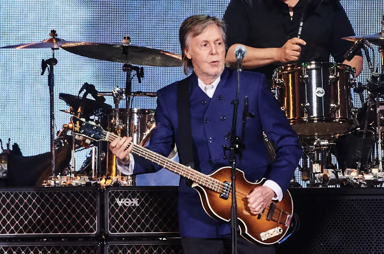 Paul McCartney joue de sa basse H&ouml;fner iconique sur sc&egrave;ne, v&ecirc;tu d'un &eacute;l&eacute;gant costume bleu.