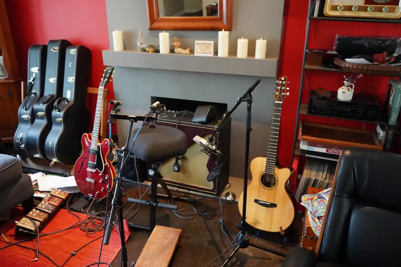 Guitare rouge et guitare acoustique en bois, prêts à enregistrer. Amplis, micros et pédales au sol.