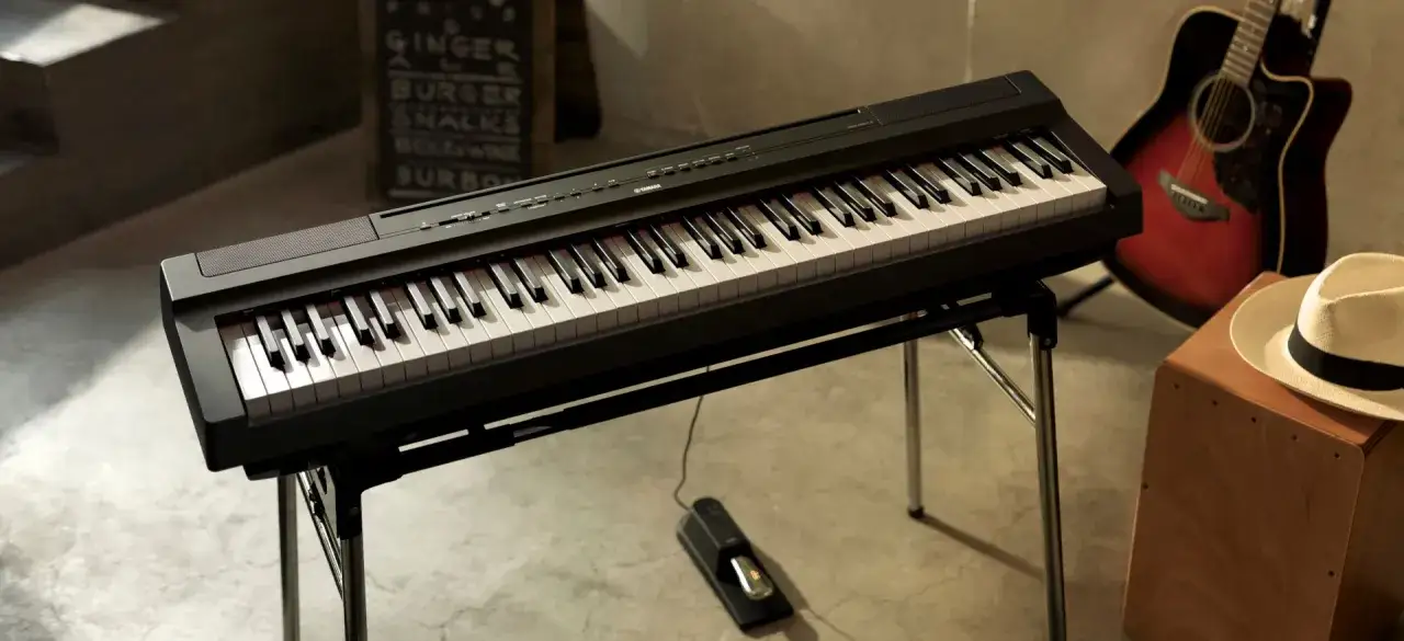 Un piano numérique noir sur un stand, prêt à jouer. Une guitare acoustique et un chapeau complètent la scène musicale.
