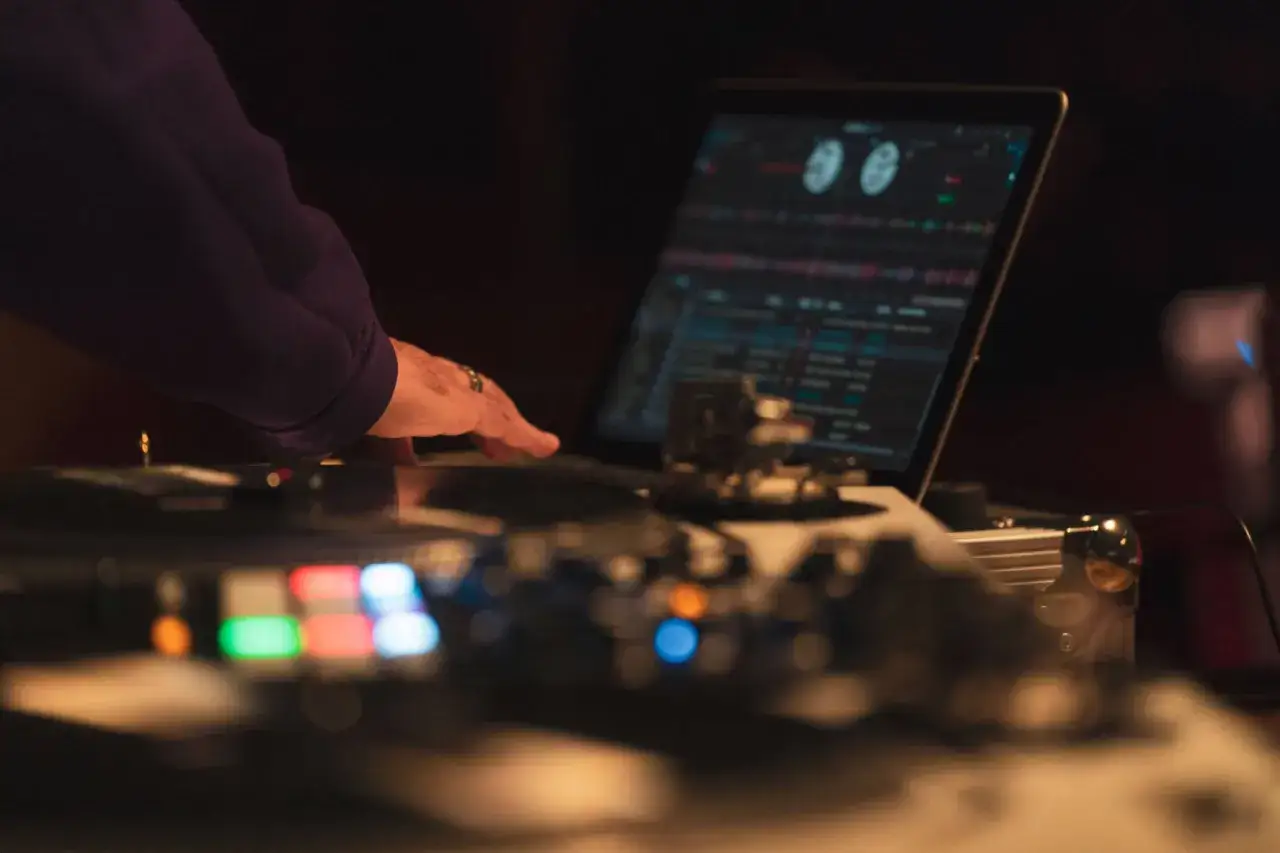 Main d'un DJ en train de faire du sampling musical sur un ordinateur portable et une table de mixage, avec des lumières colorées.