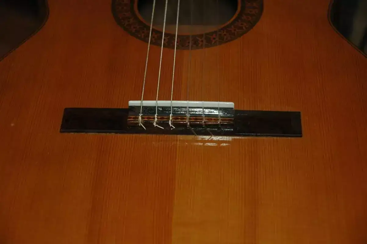 Gros plan sur le chevalet d'une guitare classique, montrant le noeud corde guitare classique et les cordes argent&eacute;es.