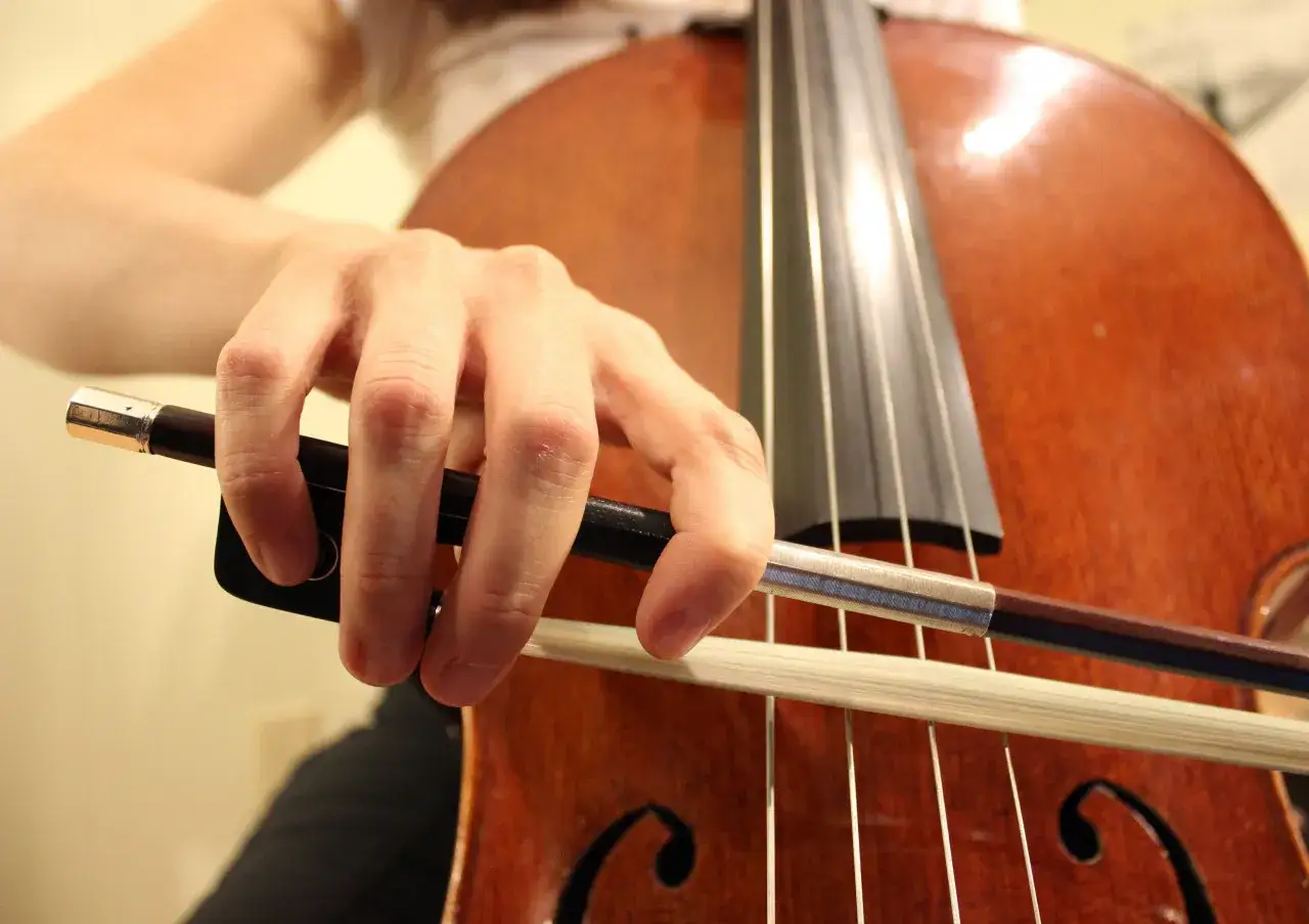 Main d'un musicien tenant un archet sur les cordes d'un violoncelle, moment cl&eacute; pour apprendre le violoncelle.